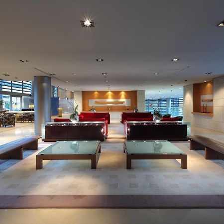 Eurostars Grand Marina Hotel Gl Barcelona Bagian luar foto The photo shows a modern and spacious interior, likely of a lobby or waiting area. It features several red sofas arranged in a conversational layout, complemented by glass-top coffee tables. The lighting is bright and there are large windows, allowin