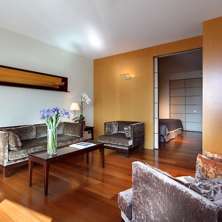 Eurostars Grand Marina Hotel Gl Barcelona Bagian luar foto The photo shows a modern living room with a warm and inviting atmosphere. It features two armchairs and a sofa, all in a plush, dark fabric. A coffee table sits in the center, with a vase of fresh flowers adding a pop of color. The room has hardwood 