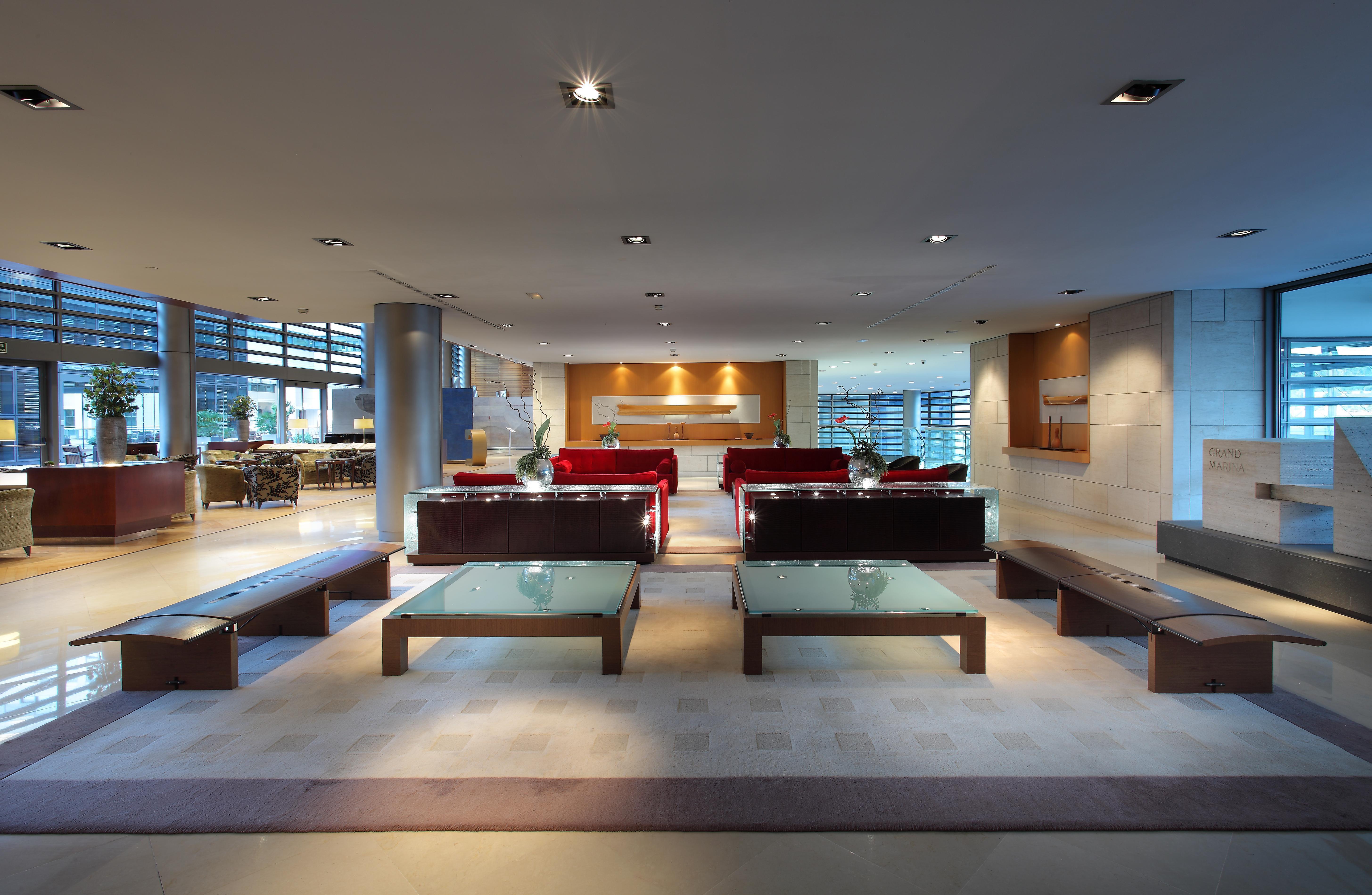 Eurostars Grand Marina Hotel Gl Barcelona Bagian luar foto The photo shows a modern and spacious interior, likely of a lobby or waiting area. It features several red sofas arranged in a conversational layout, complemented by glass-top coffee tables. The lighting is bright and there are large windows, allowin