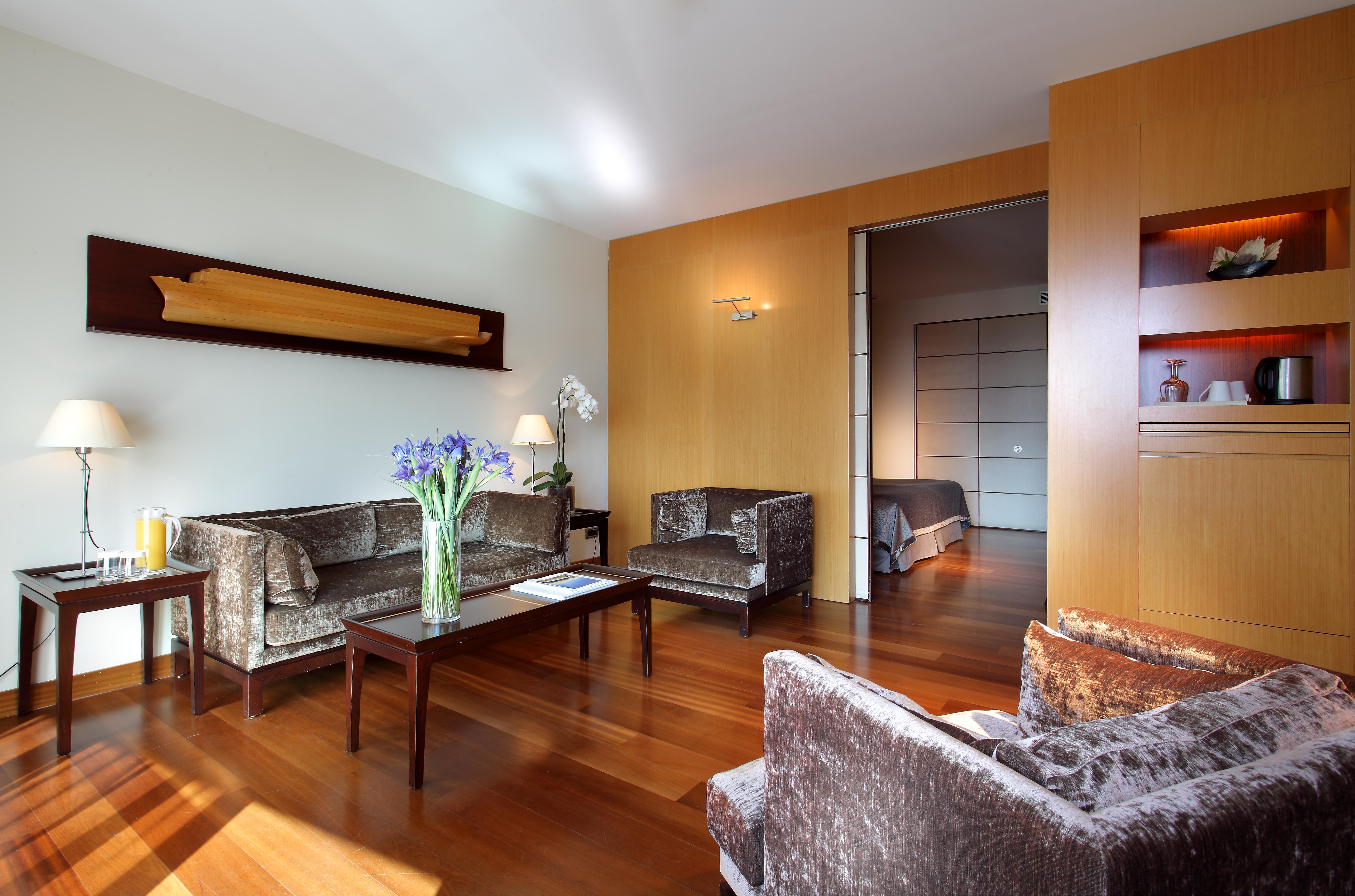 Eurostars Grand Marina Hotel Gl Barcelona Bagian luar foto The photo shows a modern living room with a warm and inviting atmosphere. It features two armchairs and a sofa, all in a plush, dark fabric. A coffee table sits in the center, with a vase of fresh flowers adding a pop of color. The room has hardwood 