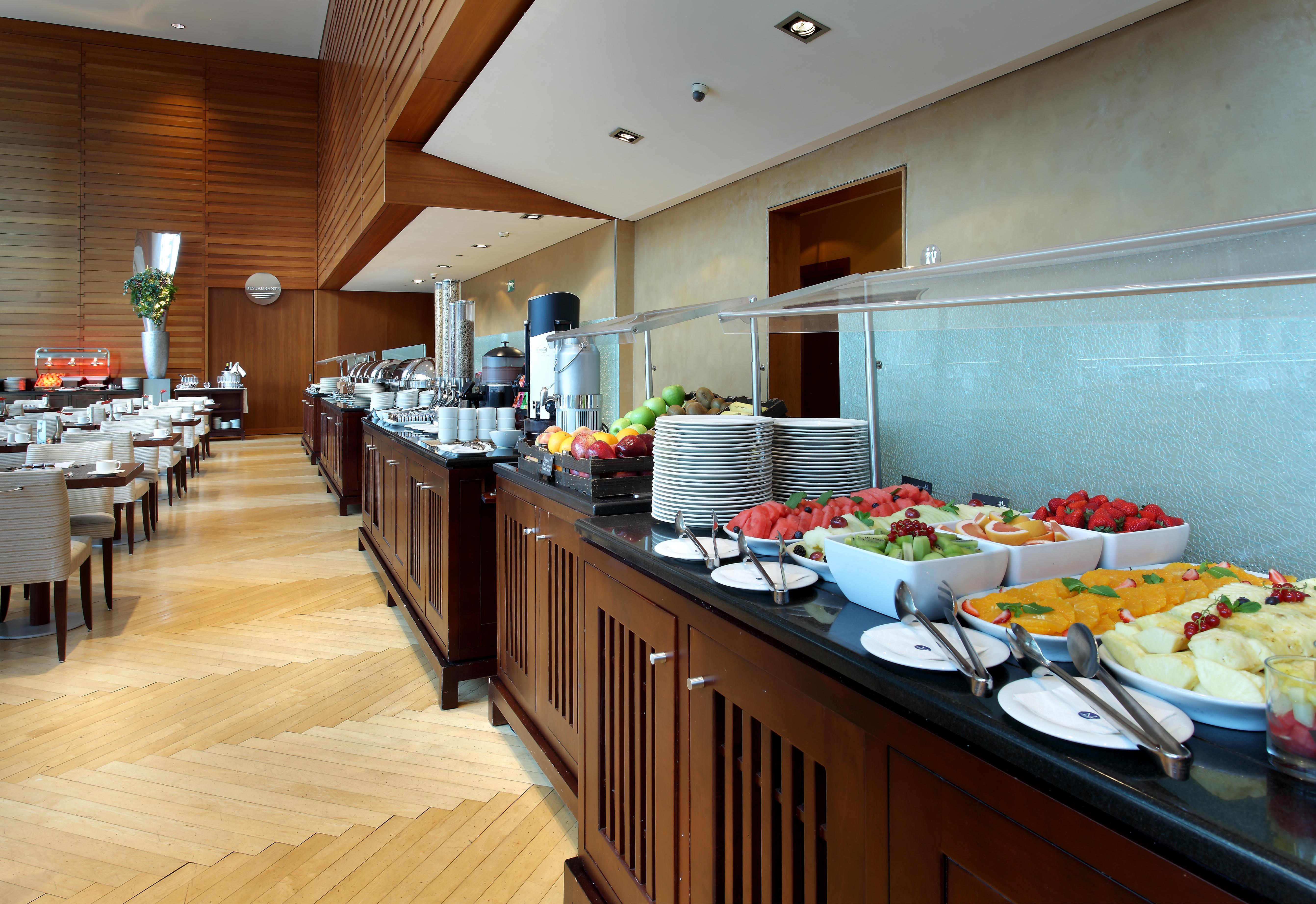 Eurostars Grand Marina Hotel Gl Barcelona Bagian luar foto The photo shows a well-organized buffet setup in a modern dining area. There is a long counter made of wood, displaying a variety of food items. Several bowls filled with fresh fruits, such as melons and strawberries, are prominently placed. In the b