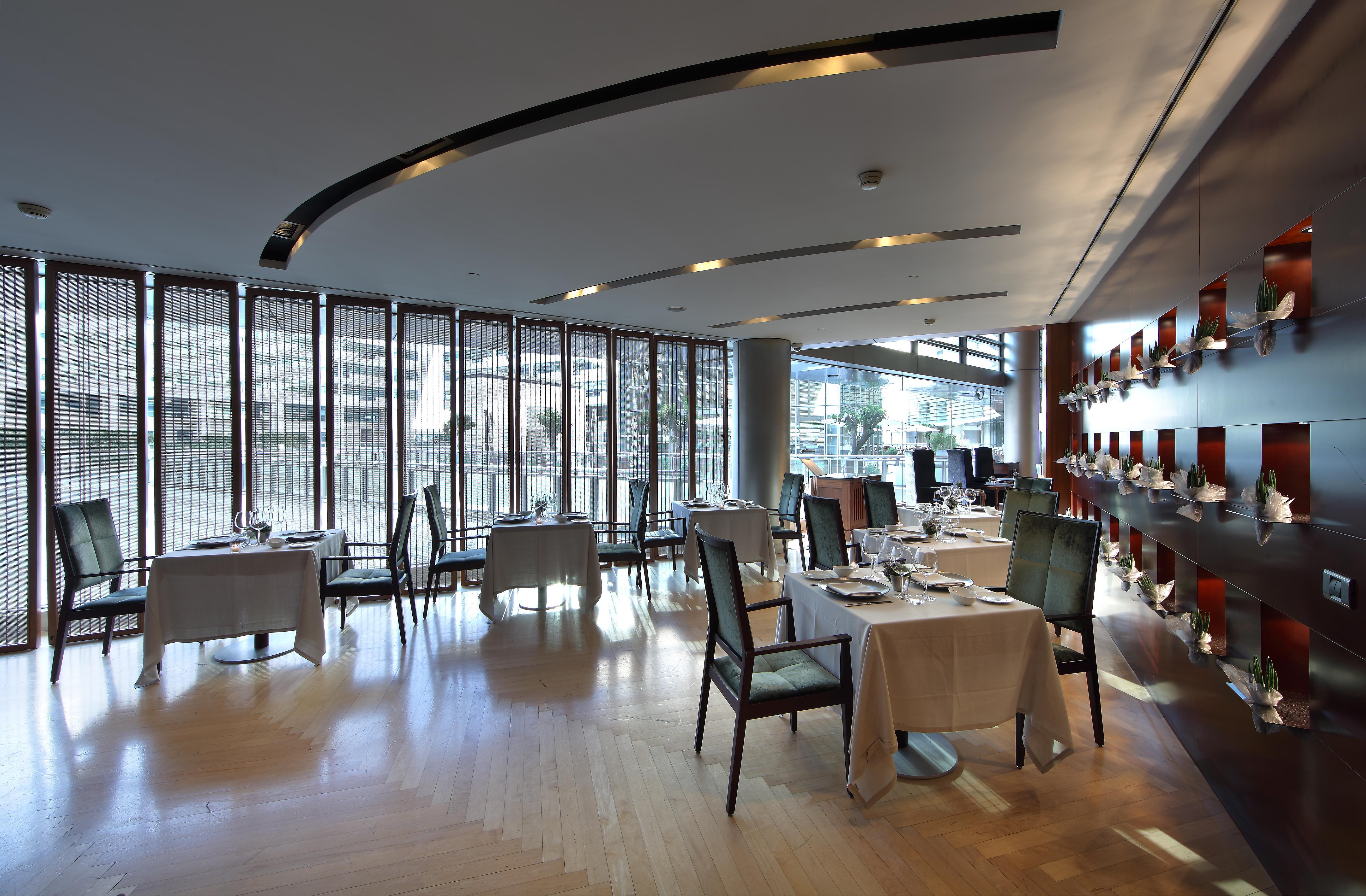 Eurostars Grand Marina Hotel Gl Barcelona Bagian luar foto The photo shows a modern and elegant restaurant interior. There are several dining tables, each covered with tablecloths and set with cutlery. The restaurant features large windows that allow natural light to illuminate the space, creating a warm atm