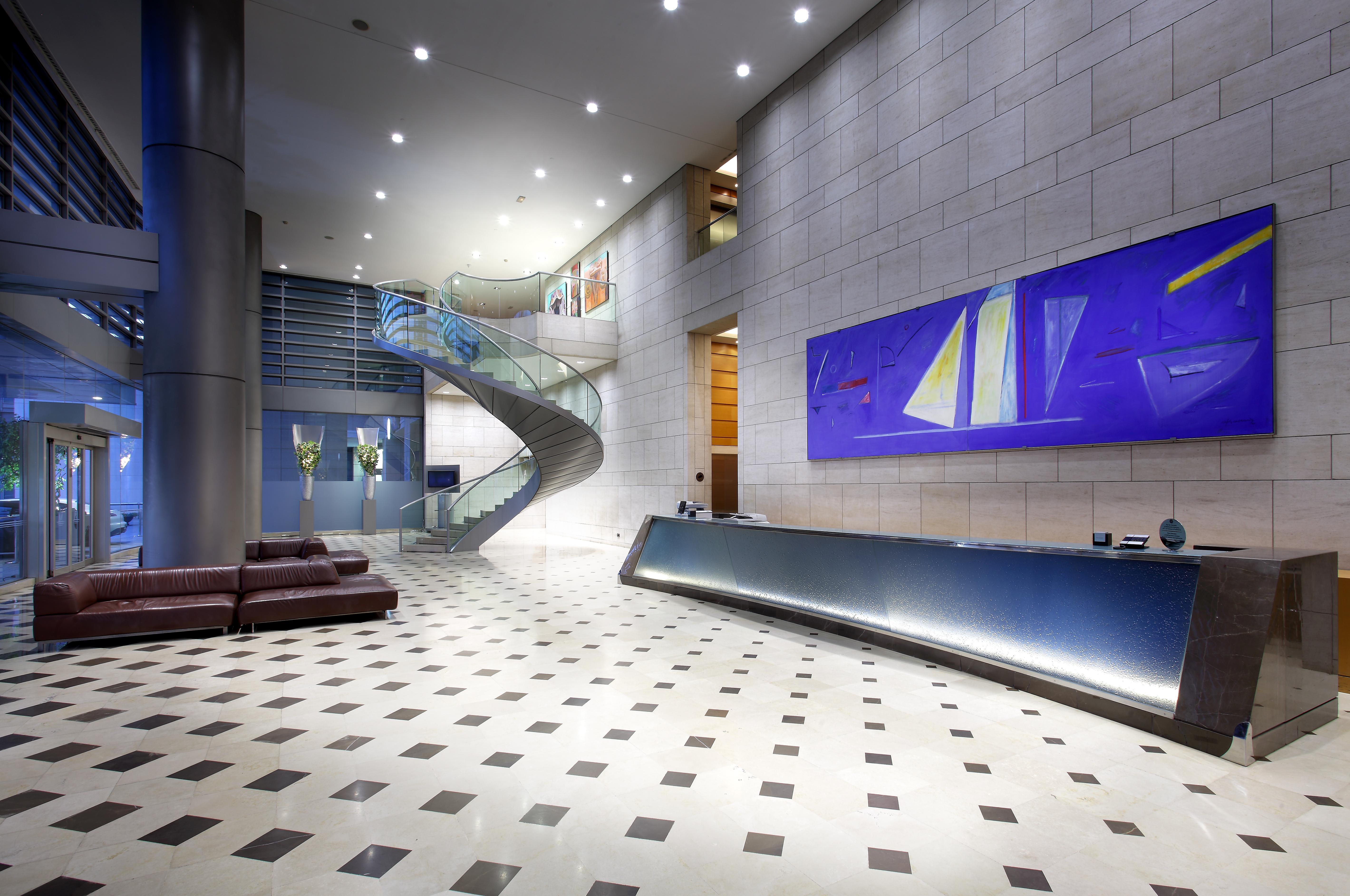 Eurostars Grand Marina Hotel Gl Barcelona Bagian luar foto The photo shows a modern lobby or reception area. There is a sleek reception desk along one wall, featuring a polished surface. To the left, a spacious staircase with a glass guardrail leading to an upper level can be seen, framed by walls decorated 