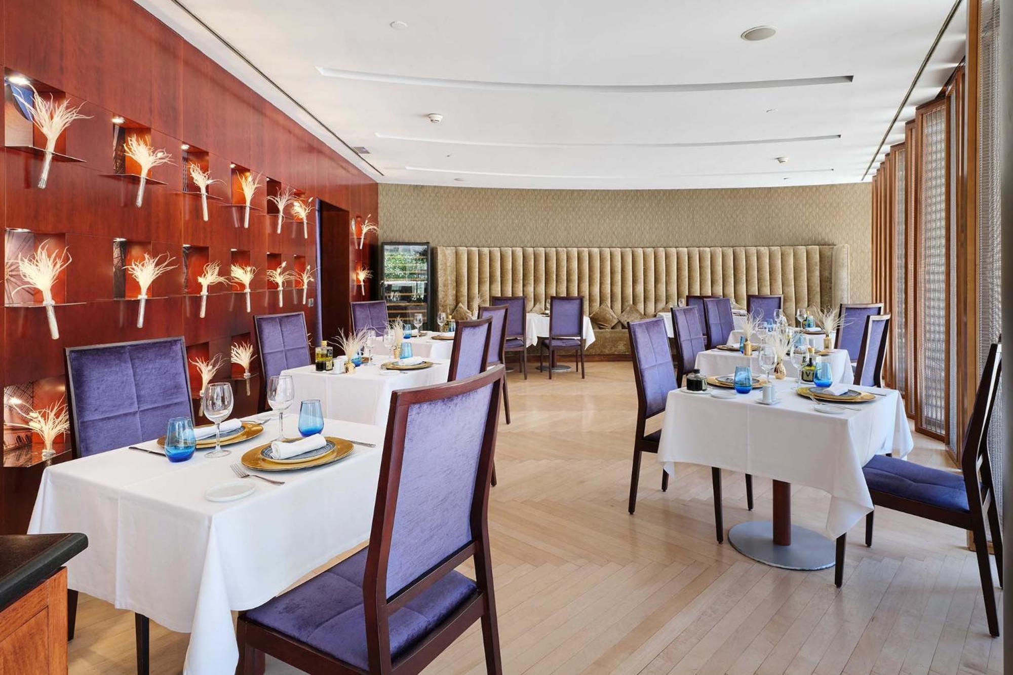 Eurostars Grand Marina Hotel Gl Barcelona Bagian luar foto The photo shows an elegant dining room in a restaurant. There are several tables set with white tablecloths, each adorned with plates, glasses, and decorative items. The chairs have a purple upholstery, adding a touch of color to the space. 

The wal